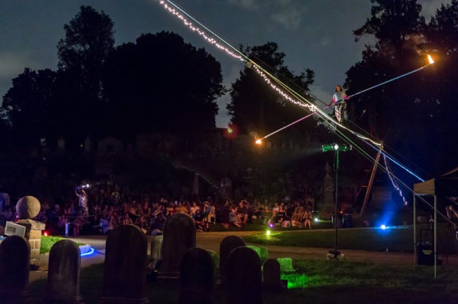 tight wire walker with fire at night with a large audience in a cemetary