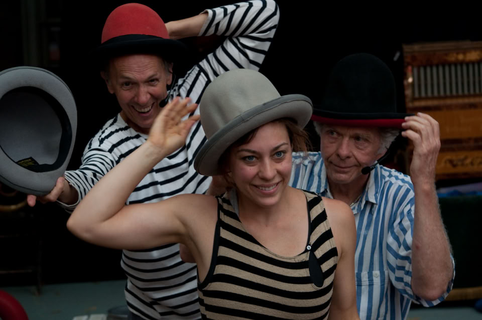 3 performers playing with multiple hats