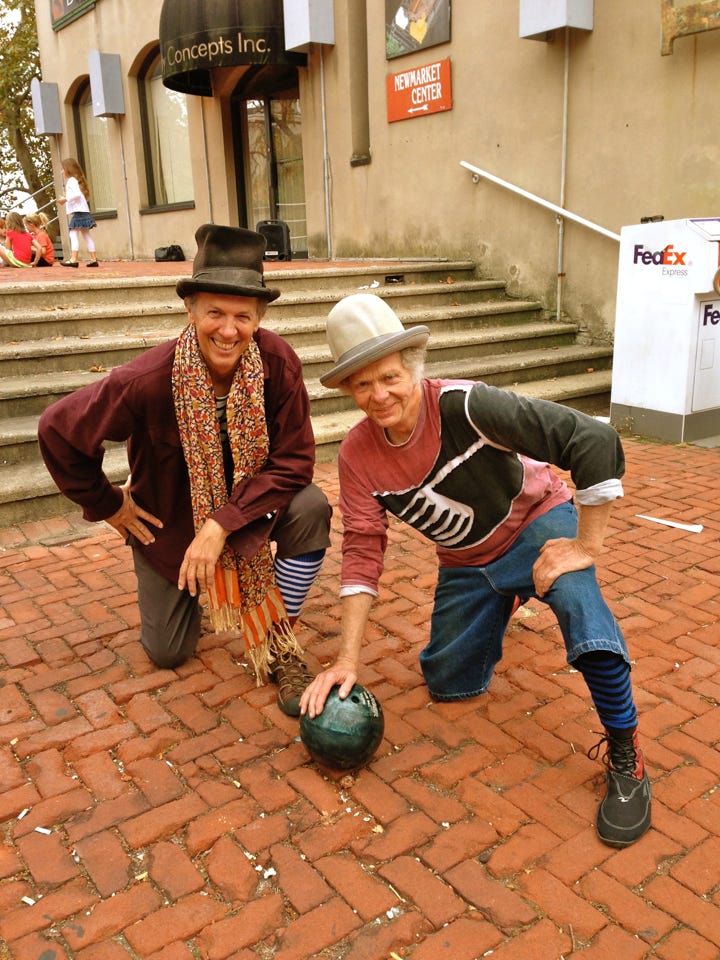 2 men smiling holding a bowling ball against a brick sidewalk