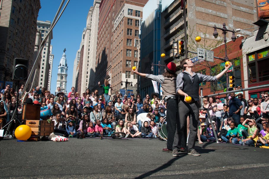 2 jugglers standing back to back juggling yellow balls street fair philadelphia