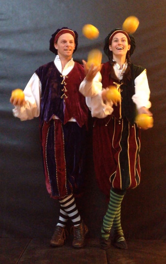 2 jugglers in velvet holiday costumes juggling yellow balls