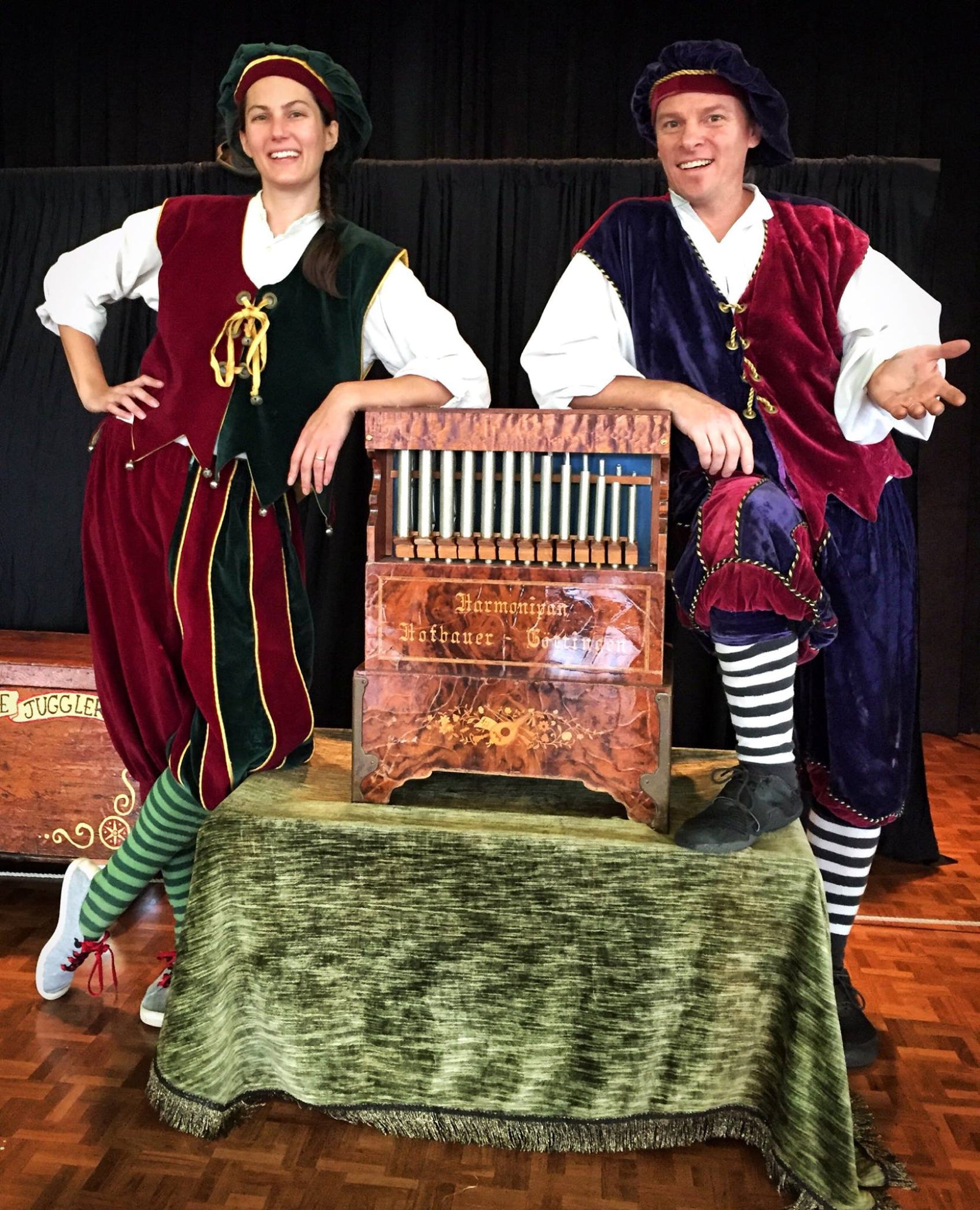 2 jugglers dressed in velvet holiday costumes standing with a calliope