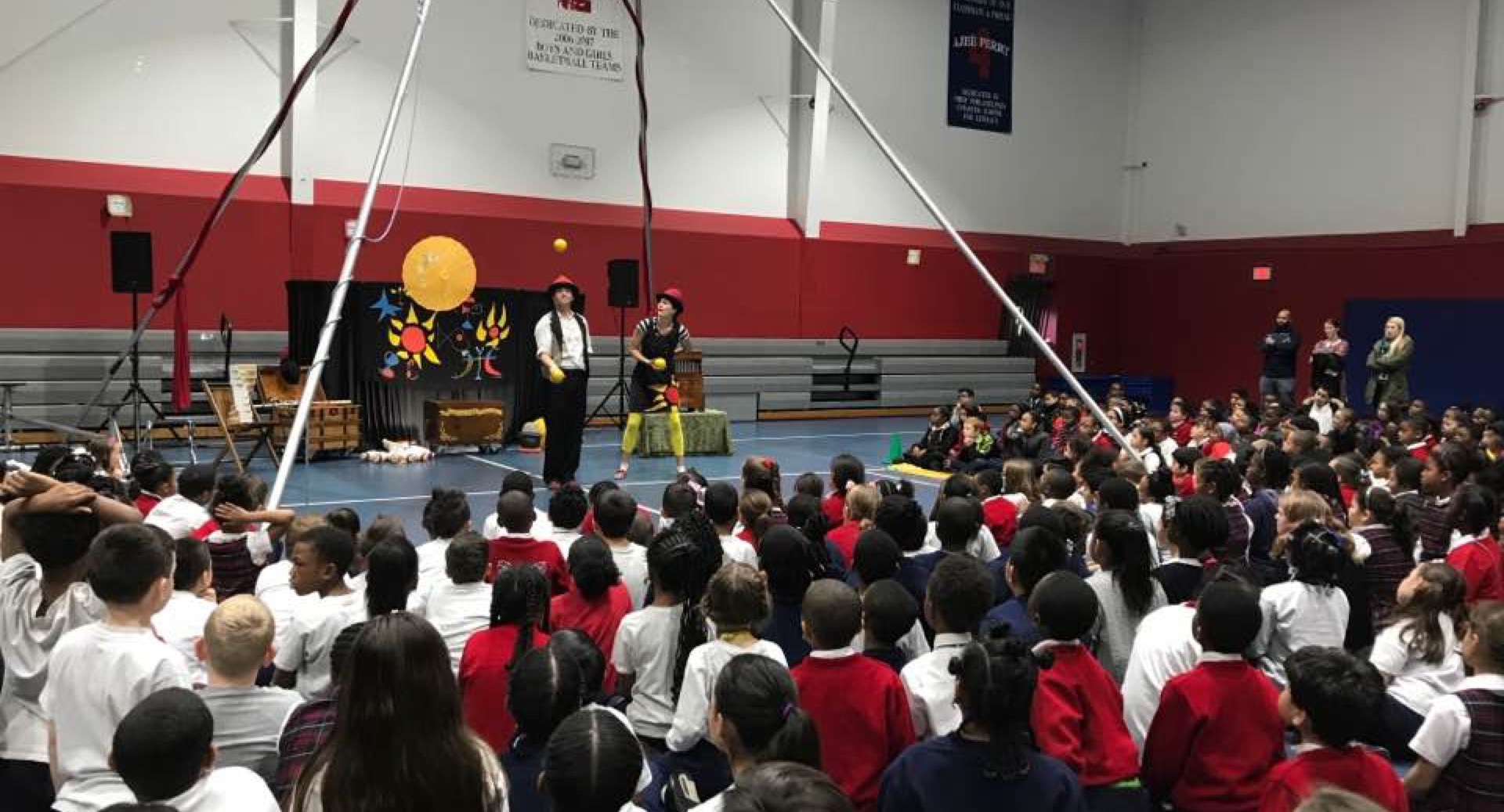 2 jugglers surrounded by a large student audience in a gym